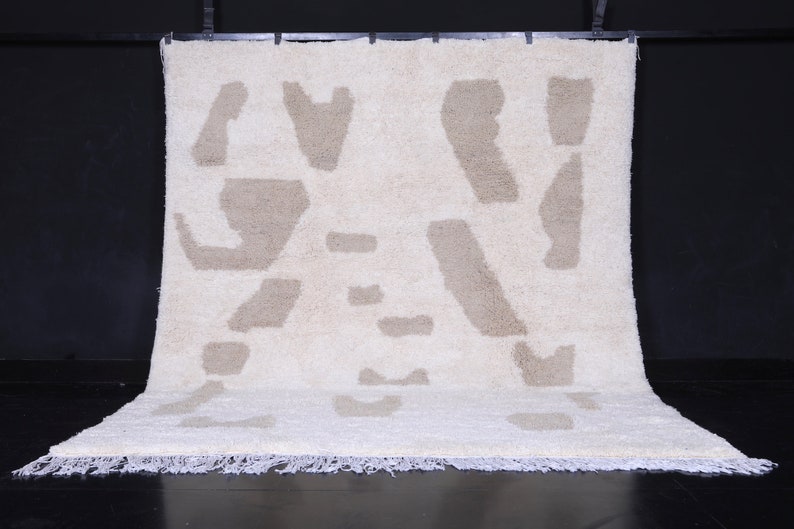 May include: A white and beige shag rug with an abstract pattern. The rug has a fringe border.