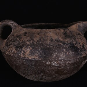 May include: A dark brown, round, ceramic pitcher with a handle and a spout. The pitcher has a rough, textured surface.