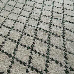 K&ouml;nnte beinhalten: Cremefarbener Teppich mit einem geometrischen Rautenmuster. Das Design weist dunkelgr&uuml;ne Akzente innerhalb der Rautenformen auf und erzeugt ein strukturiertes, weiches Aussehen. Die neutralen T&ouml;ne und das Muster des Teppichs eignen sich f&uuml;r verschiedene Einrichtungsstile.