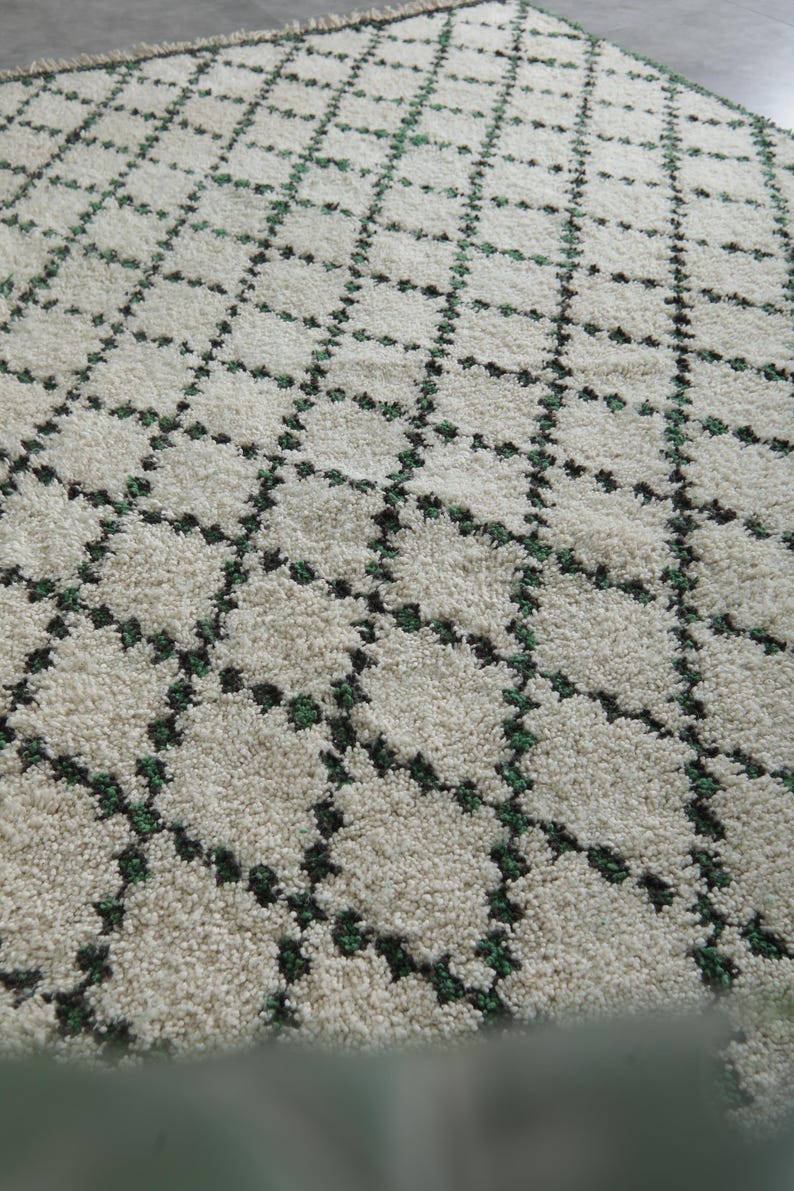 K&ouml;nnte beinhalten: Cremefarbener Teppich mit einem geometrischen Rautenmuster. Das Design weist dunkelgr&uuml;ne Akzente innerhalb der Rautenformen auf und erzeugt ein strukturiertes, weiches Aussehen. Die neutralen T&ouml;ne und das Muster des Teppichs eignen sich f&uuml;r verschiedene Einrichtungsstile.