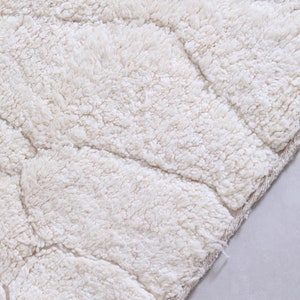 May include: A close-up of a white, fluffy bath mat with a textured, wave-like pattern. The mat has a soft, plush feel and is perfect for adding comfort and style to any bathroom.