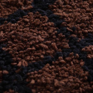 Peut inclure: Gros plan sur un tapis textur&eacute; avec un motif r&eacute;p&eacute;titif. Le tapis pr&eacute;sente une combinaison de couleurs marron et noir, cr&eacute;ant un design visuellement int&eacute;ressant. La texture semble douce et moelleuse.