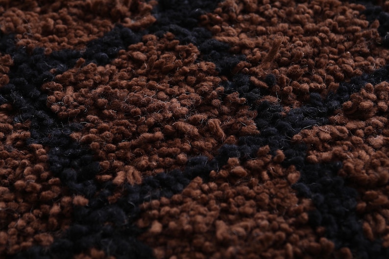 Peut inclure: Gros plan sur un tapis textur&eacute; avec un motif r&eacute;p&eacute;titif. Le tapis pr&eacute;sente une combinaison de couleurs marron et noir, cr&eacute;ant un design visuellement int&eacute;ressant. La texture semble douce et moelleuse.