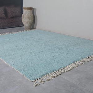 May include: A light blue rug with a white fringe border. The rug is made of a soft, fluffy material and has a subtle texture.