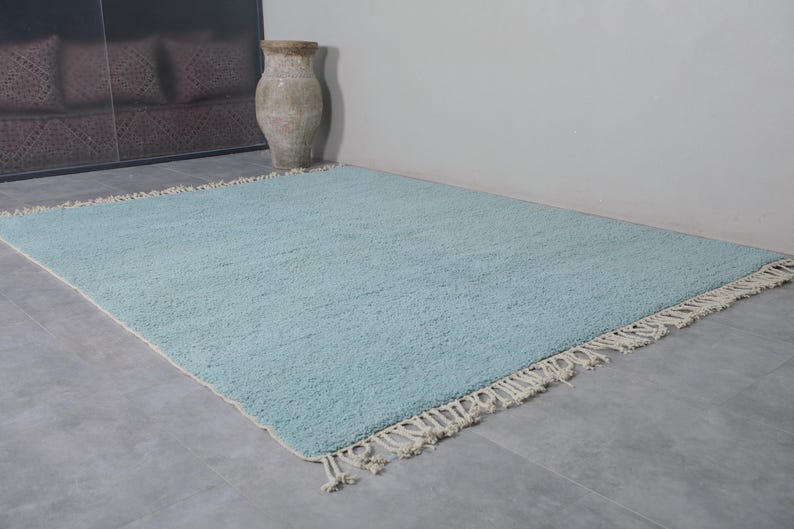 May include: A light blue rug with a white fringe border. The rug is made of a soft, fluffy material and has a subtle texture.