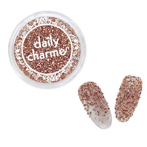 May include: A small jar of rose gold glitter with the text "daily charmes" on the label. Two nails are decorated with the glitter.