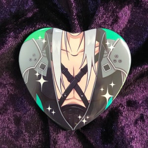 May include: A heart-shaped button featuring a character with long white hair, wearing a black outfit with a cross-shaped strap design. The character has a light green background with sparkling accents.