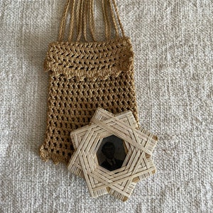 May include: A brown crocheted bag with a wooden star-shaped frame holding a black and white photo of a man. The bag has a white wooden ring at the top.