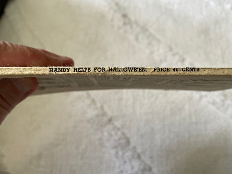 May include: Close-up of the bottom edge of a vintage book with the text "HANDY HELPS FOR HALLOWEEN. PRICE 40 CENTS."