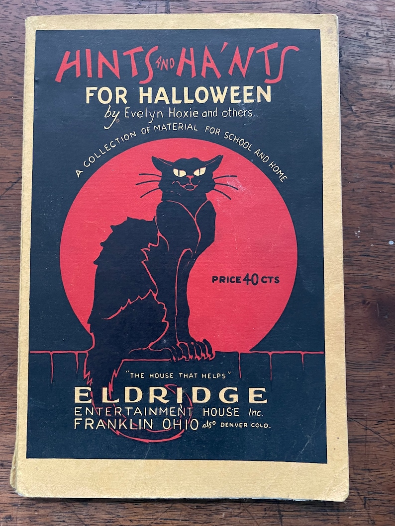 May include: A vintage book cover with a black cat silhouette against a red circle. The title is "Hints and Ha'nts for Halloween" by Evelyn Hoxie and others. The book is a collection of material for school and home. The price is 40 cents. The publisher is Eldridge Entertainment House Inc. in Franklin, Ohio and Denver, Colorado.