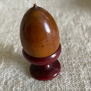 May include: A wooden acorn-shaped trinket box with a dark red base. The box is closed and has a smooth, polished finish.