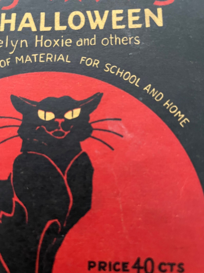 May include: A vintage book cover with a black cat silhouette against a red background. The title is "Halloween" in gold lettering. The text "Elyn Hoxie and others" is below the title. The text "of material for school and home" is below the cat. The text "Price 40 cts" is at the bottom of the cover.