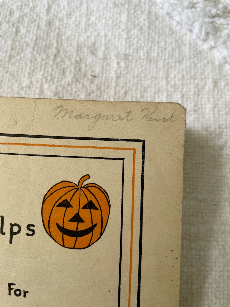 May include: A vintage Halloween card with an orange pumpkin with a black smiling face. The card has a black border and the text "Helps" and "For" are visible. The card is signed "Margaret Kennard".