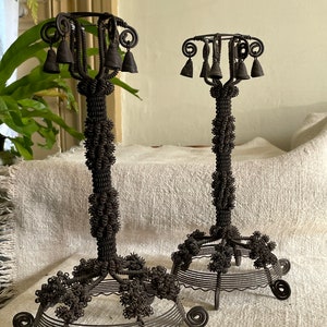 May include: Two antique wire candle holders with bells. The holders are made of twisted wire and have a decorative design. The bells are attached to the top of the holders.