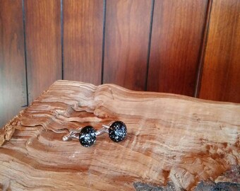 May include: A pair of black cufflinks with white speckles, set on a piece of weathered wood.