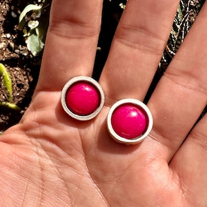 Op de afbeelding: Een paar zilveren oorbellen met ronde roze cabochons.