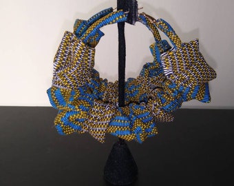 May include: A pair of large hoop earrings made of blue and yellow patterned fabric. The earrings are displayed on a black stand.