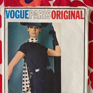 Puede incluir: Patrón de costura Vogue Paris Original número 1489 de Molyneux. El patrón presenta una bufanda de lunares negros y blancos y un vestido negro con cinturón.