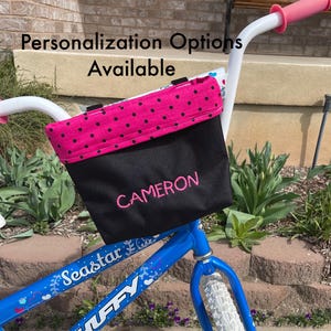 May include: A blue bicycle with a black and pink polka dot handlebar bag. The bag is personalized with the name "CAMERON".