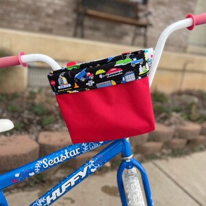 May include: A blue bicycle with a red and black handlebar basket. The basket has a black and white fabric lining with a pattern of construction vehicles. The bicycle has white tires and a white handlebar. The bicycle has the words "Seastar" and "HUFFY" printed on the frame.