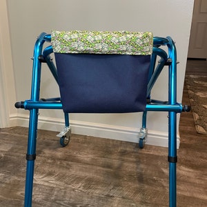 May include: A blue walker with a navy blue fabric bag attached. The bag has a green and white patterned top with cartoon characters.
