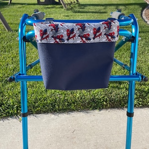 May include: A blue walker with a navy blue and white fabric bag attached. The bag has a Spiderman pattern on the top and a solid navy blue bottom.