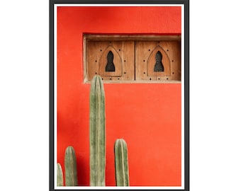 May include: A bright red wall with a wooden window featuring two arched openings. Three tall green cacti are in front of the wall.