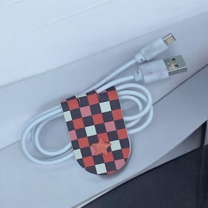May include: White charging cable with a black and red checkered cable organizer with a red star.