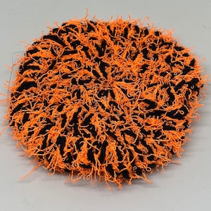 May include: A black and orange fluffy round rug with a textured, shaggy surface.