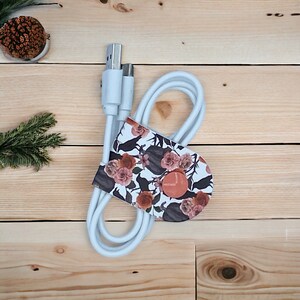 May include: White USB charging cable with a floral and bird print cable organizer. The organizer has a button closure and a brown button.