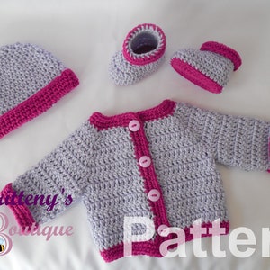 May include: A crocheted baby outfit in lavender and pink. The set includes a hat, cardigan, and booties. The cardigan has a button closure and pink trim. The hat and booties also have pink trim.