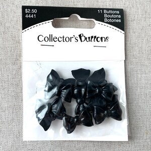 May include: A package of 11 black bow-shaped buttons. The package is labeled "Collector's Buttons" and has a price tag of $2.50. The buttons are made of plastic and have a shiny finish.