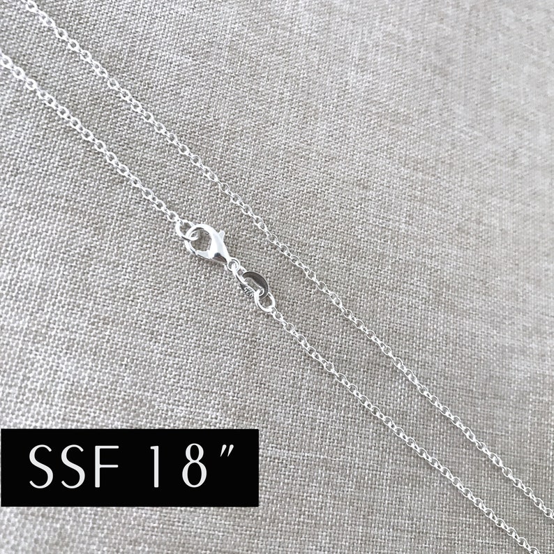 May include: A silver chain necklace with a lobster clasp. The chain is 18 inches long and is displayed on a fabric background. SSF 18"
