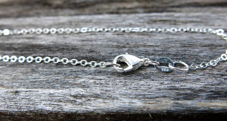 May include: A silver chain necklace with a lobster clasp closure. The clasp is stamped with "925", indicating that the necklace is made of sterling silver.