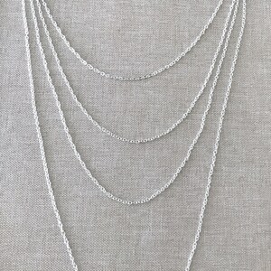 May include: A silver chain necklace with multiple strands of varying lengths. The necklace is layered and hangs in a cascading pattern.