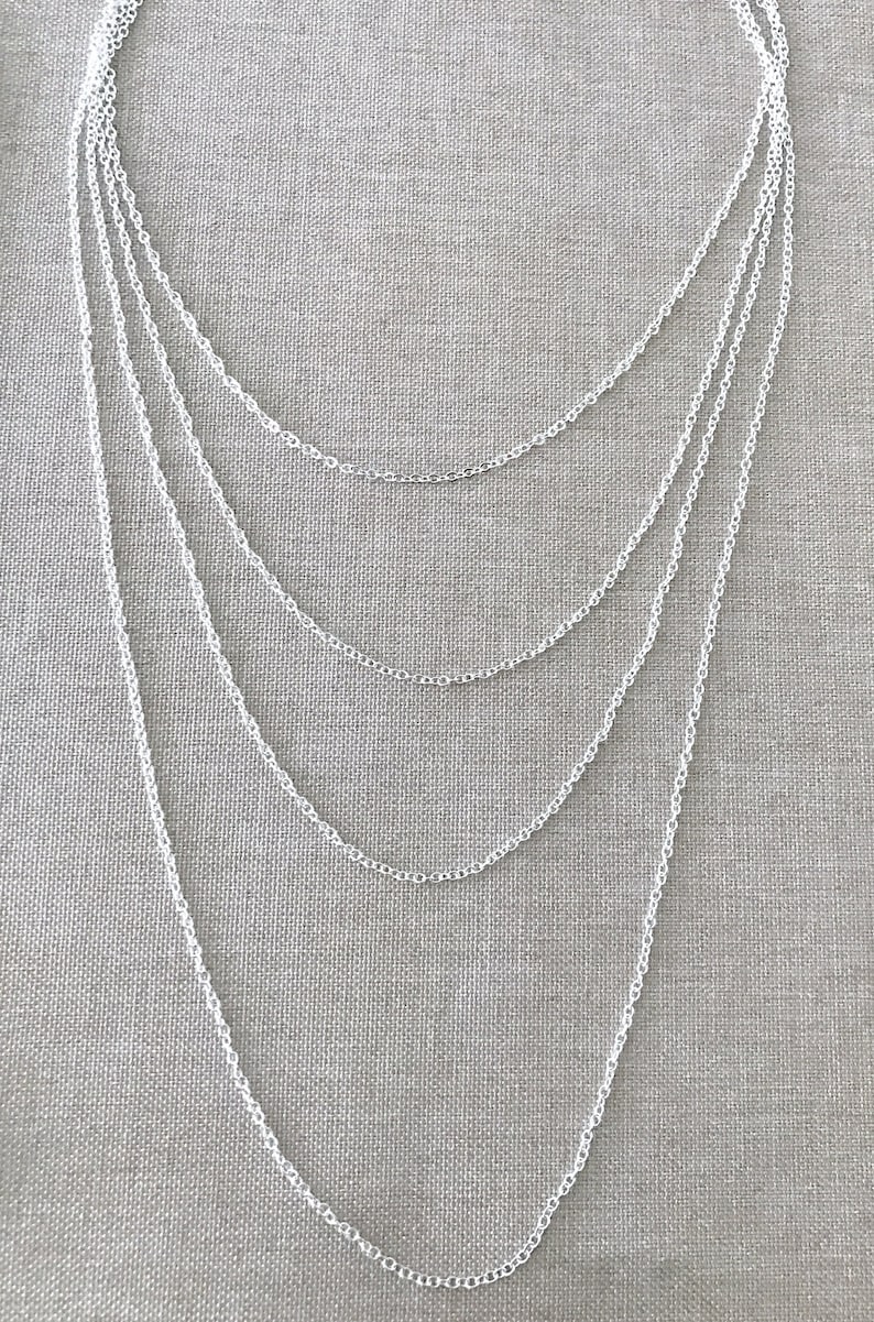 May include: A silver chain necklace with multiple strands of varying lengths. The necklace is layered and hangs in a cascading pattern.