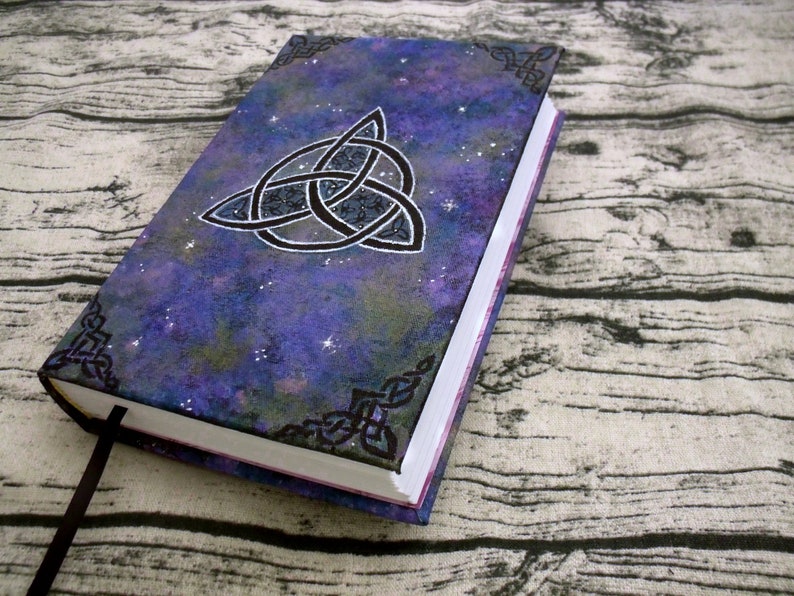 May include: A purple and black journal with a silver Celtic knot design on the cover. The cover has a galaxy-like pattern with white stars.