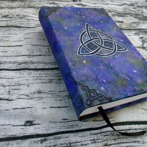 May include: A purple and blue notebook with a silver glitter finish. The cover features a black Celtic knot design and a starry night sky background.
