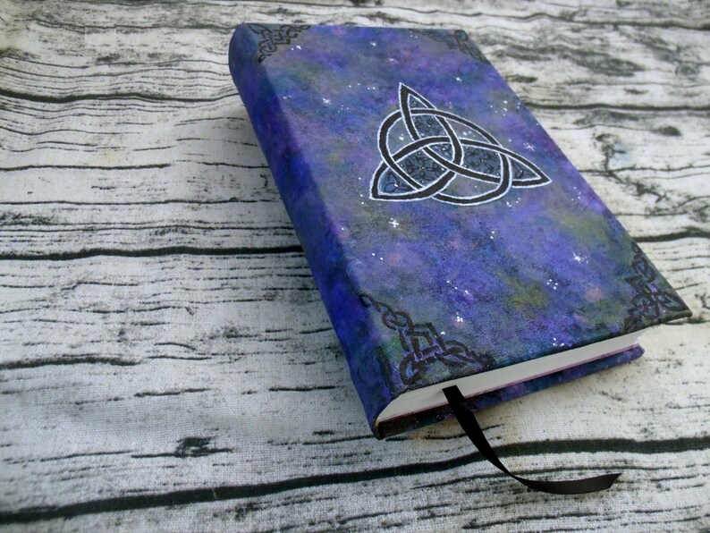 May include: A purple and blue notebook with a silver glitter finish. The cover features a black Celtic knot design and a starry night sky background.