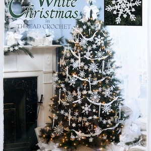 May include: A Christmas tree decorated with white thread crochet snowflakes and ornaments. The book cover in the background reads "White Christmas in Thread Crochet" with the Leisure Arts logo. The book cover also shows a white wreath and gifts.