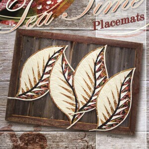 May include: A set of four leaf-shaped quilted placemats featuring cream-colored fabric with dark brown and multi-colored autumn leaf patterns. The product packaging displays the text Tea Time Placemats, Timeless Treasures, and Quiltworx.com.