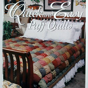May include: A book cover titled "Quick and Easy Puff Quilts" featuring a bed with a colorful patchwork quilt. The quilt has a textured, three-dimensional appearance with various plaid and solid fabric squares. White pillows and a ruffled bed skirt are also visible.