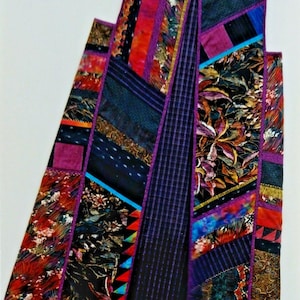 May include: A sleeveless vest constructed from a patchwork of various fabric strips in shades of purple, red, blue, and black. The garment features a mix of floral, plaid, and solid patterns, all joined together with visible purple fabric seams.