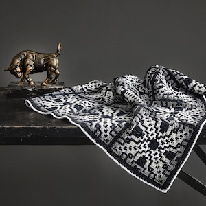 Puede incluir: Una manta de tiro con estampado en blanco y negro con un borde blanco, drapeada sobre una mesa negra con una figura de toro de bronce sobre una base negra.