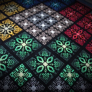 Puede incluir: Una manta de ganchillo colorida con un patrón geométrico de cuadrados y flores. La manta está hecha con una variedad de colores, incluyendo negro, verde, amarillo, rojo y blanco.