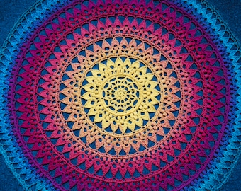 Może przedstawiać: Kolorowe, szydełkowe mandala z tęczowym gradientem od niebieskiego, fioletowego, różowego, pomarańczowego do żółtego. Mandala wykonana jest z powtarzającego się wzoru małych ściegów i ma okrągły kształt.