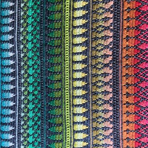 Op de afbeelding: Close-up van een kleurrijk textiel met verticale strepen. Het ontwerp toont een verloop van kleuren, waaronder blauw, groen, geel, oranje en roze. Het patroon bevat bladachtige vormen en geometrische ruitpatronen, wat een textuur cre&euml;ert.