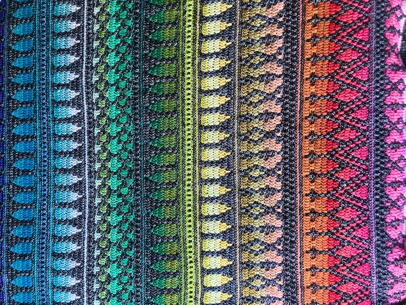 Op de afbeelding: Close-up van een kleurrijk textiel met verticale strepen. Het ontwerp toont een verloop van kleuren, waaronder blauw, groen, geel, oranje en roze. Het patroon bevat bladachtige vormen en geometrische ruitpatronen, wat een textuur cre&euml;ert.
