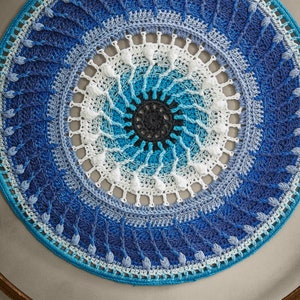 May include: A blue and white crocheted mandala with a circular design. The mandala is hanging on a wooden hoop.