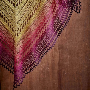 May include: A crocheted shawl with a gradient of yellow, orange, red, and purple colors. The shawl is draped over a wooden surface.